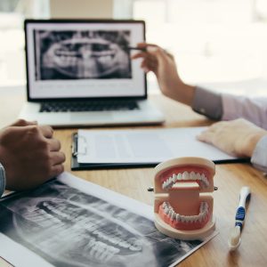 Dentists are discussing dental problems at report x-ray image on laptop screen to patients.